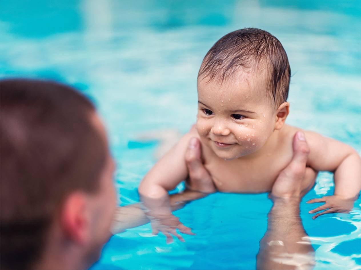 Baby schwimmt mit einem Erwachsenen im Pool.