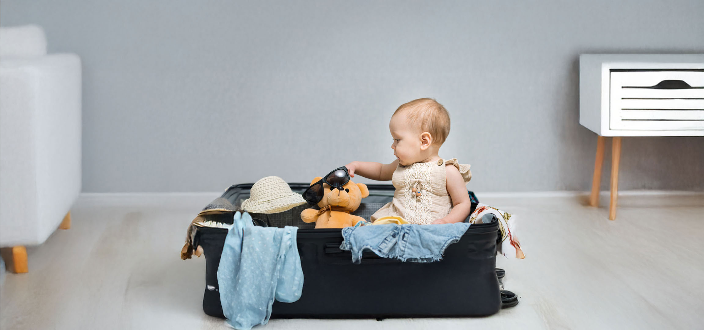Ein Baby packt Kleidung und einen Teddy in einen Koffer.