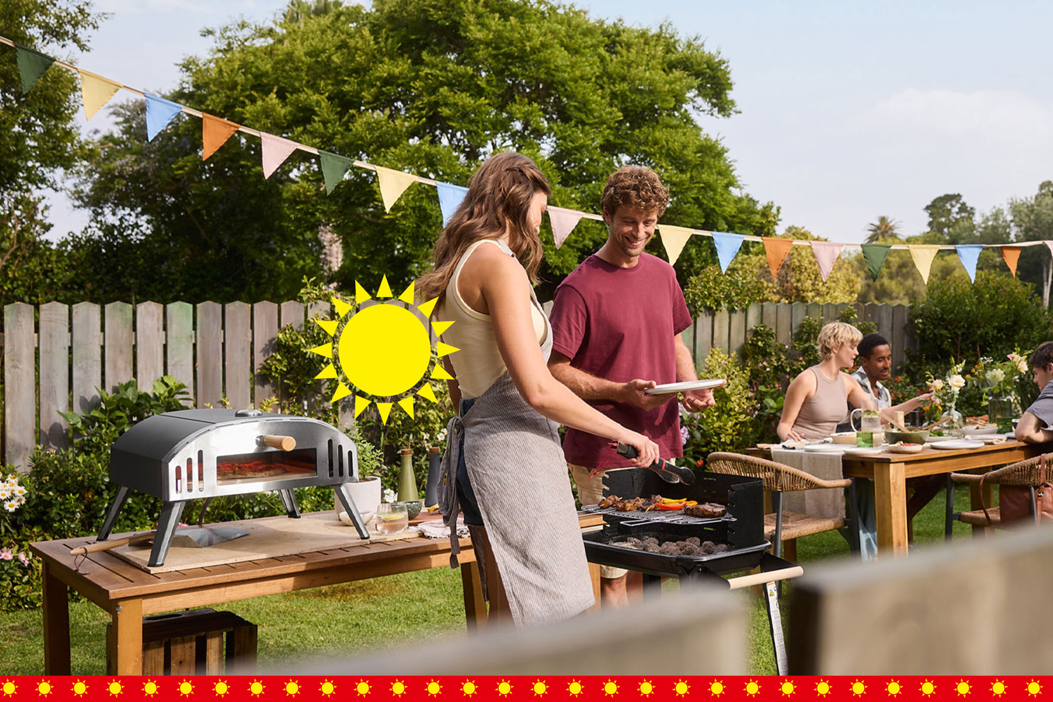 Paar grillt Pizza im Garten, Freunde sitzen am Tisch, bunte Wimpelkette, Sonne. AI-generiert
