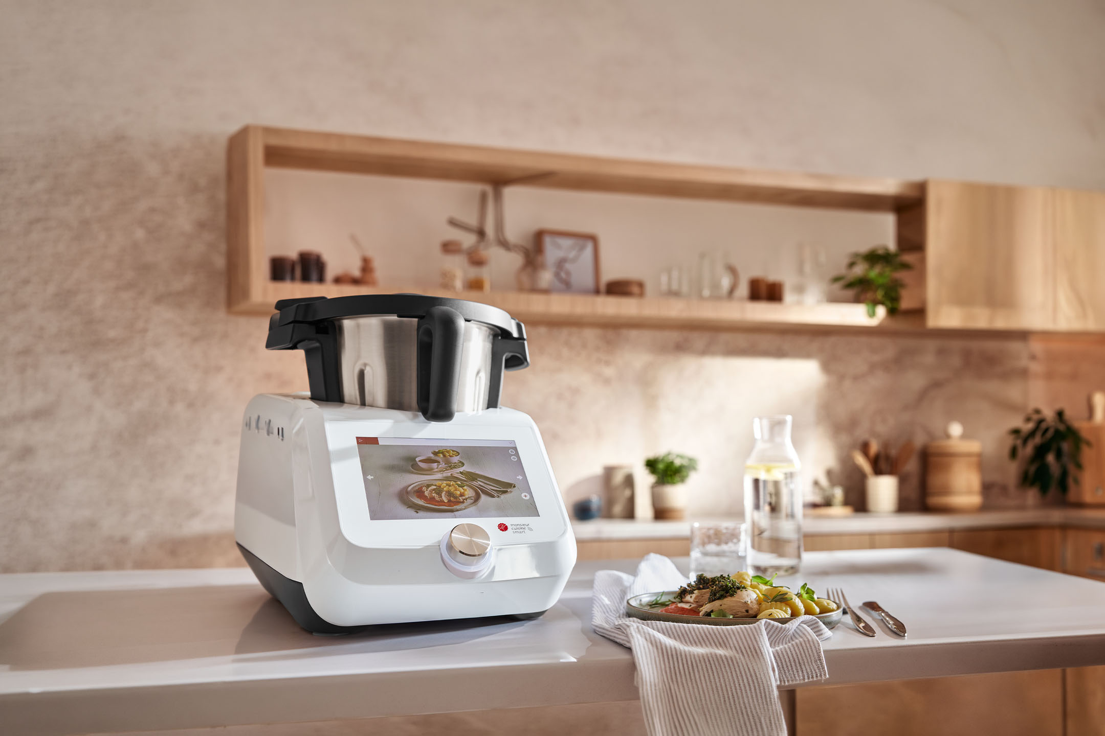 Intelligentes Küchengerät auf einer Arbeitsplatte mit zubereitetem Essen und Wasserflasche in einer modernen Küche.