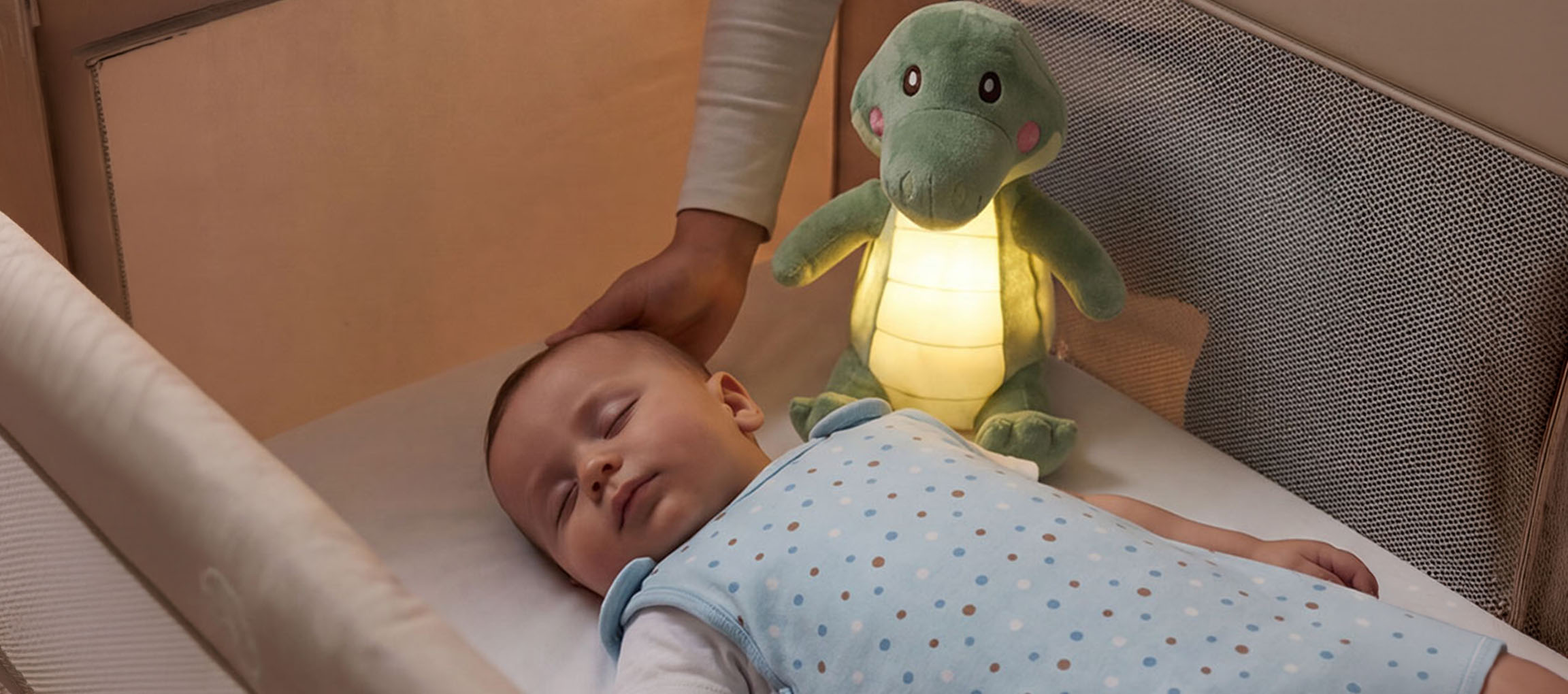 Baby schläft im Kinderbett mit Plüsch-Nachtlicht, Erwachsener streichelt den Kopf des Babys.