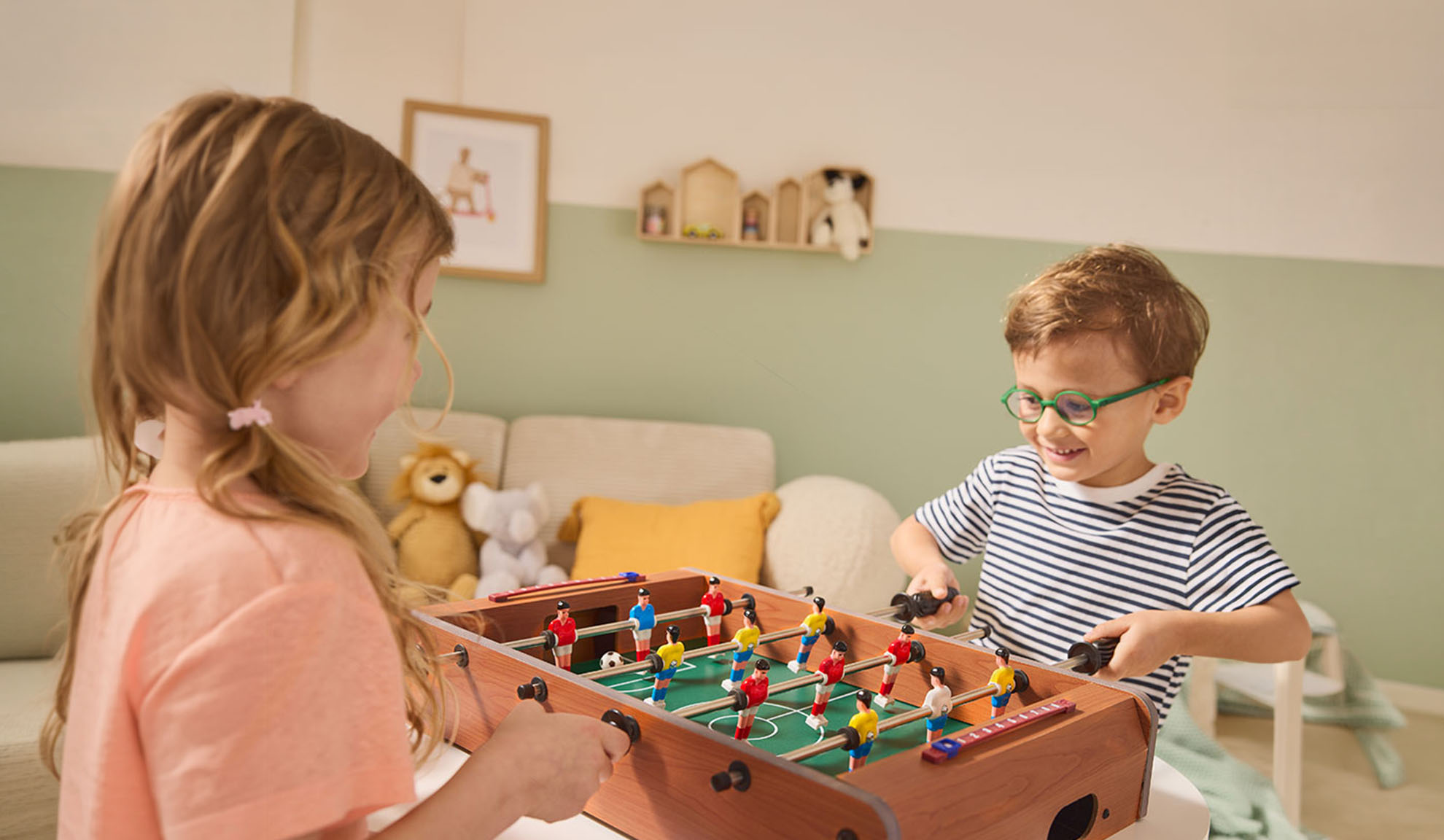 Zwei Kinder spielen Tischfußball und lachen fröhlich.