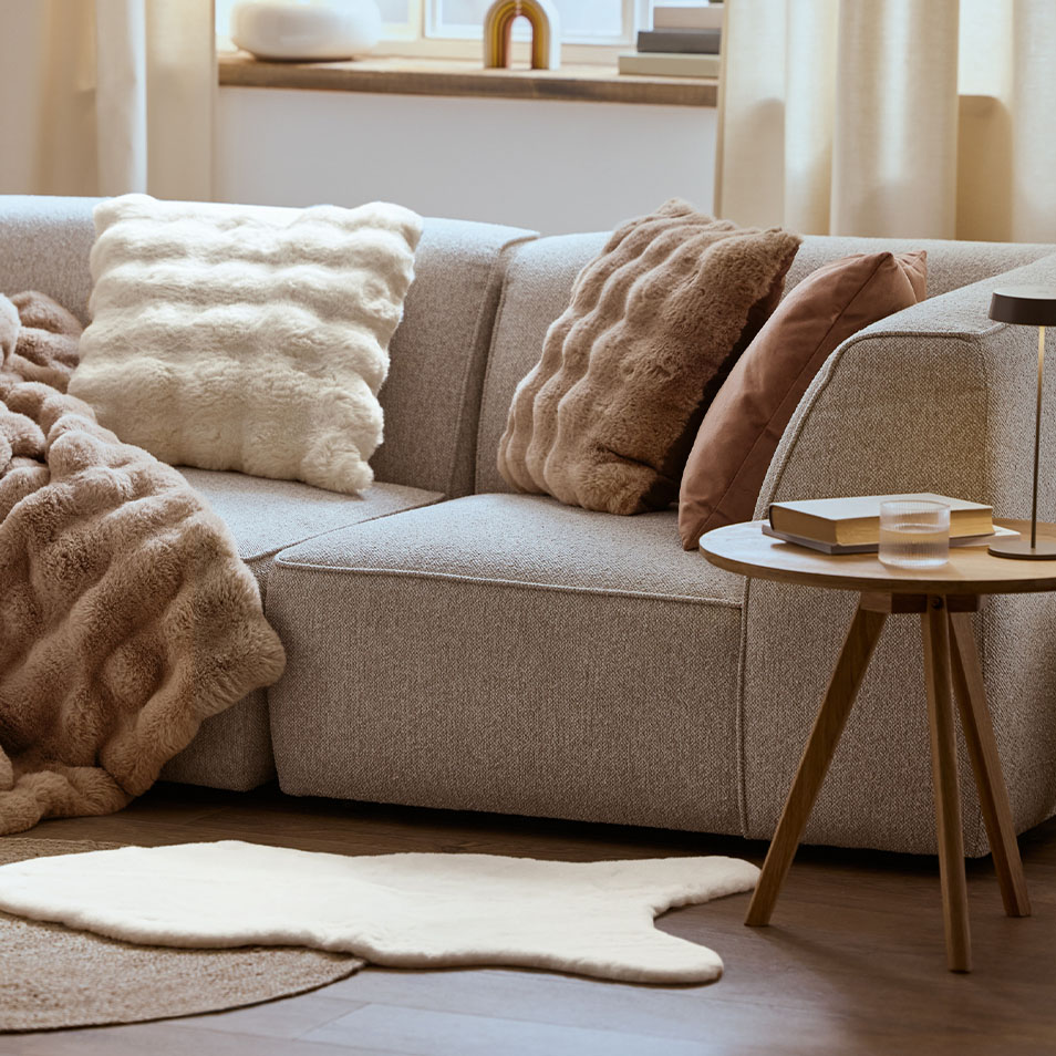 Graues Modulsofa mit flauschigen Kissen und Decken, neben einem Couchtisch.