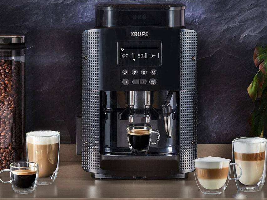 Eine schwarze Krups Kaffeemaschine mit Tassen Kaffee und Bohnenbehälter.