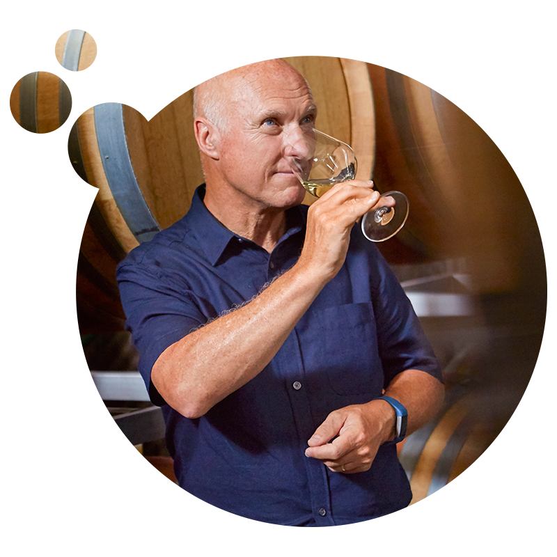 Ein Mann verkostet Weißwein in einem Weinkeller mit Holzfässern.