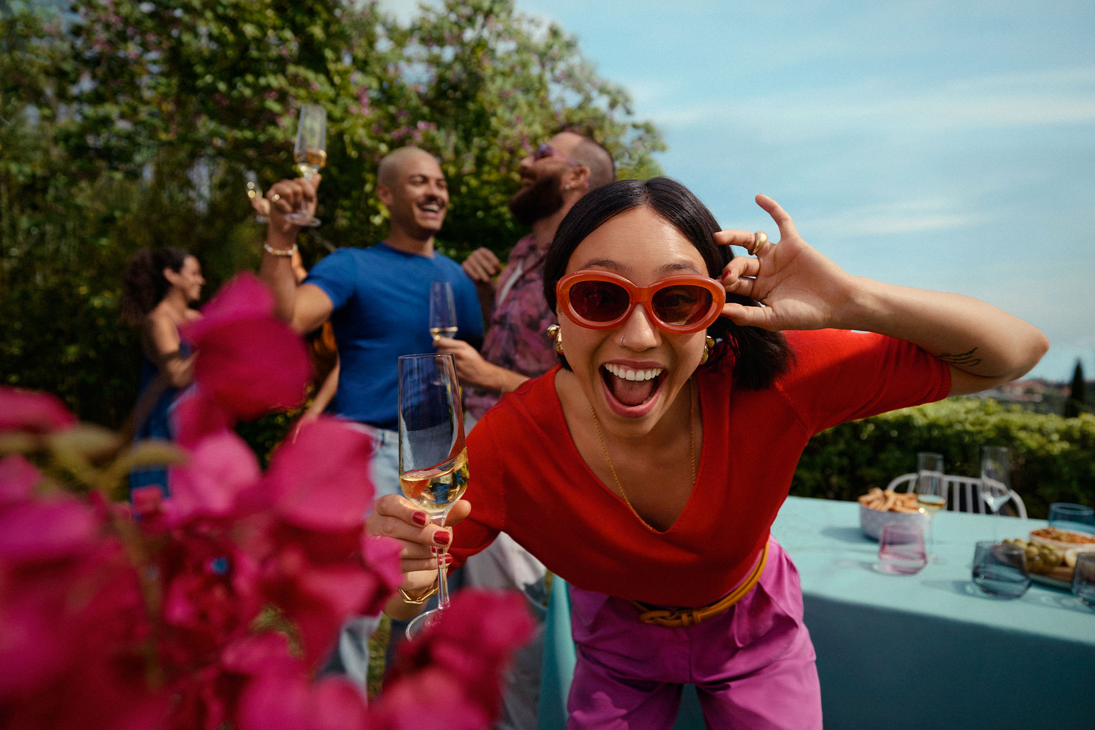 Fröhliche Frau mit Sonnenbrille und Sektglas auf einer Gartenparty mit Freunden.