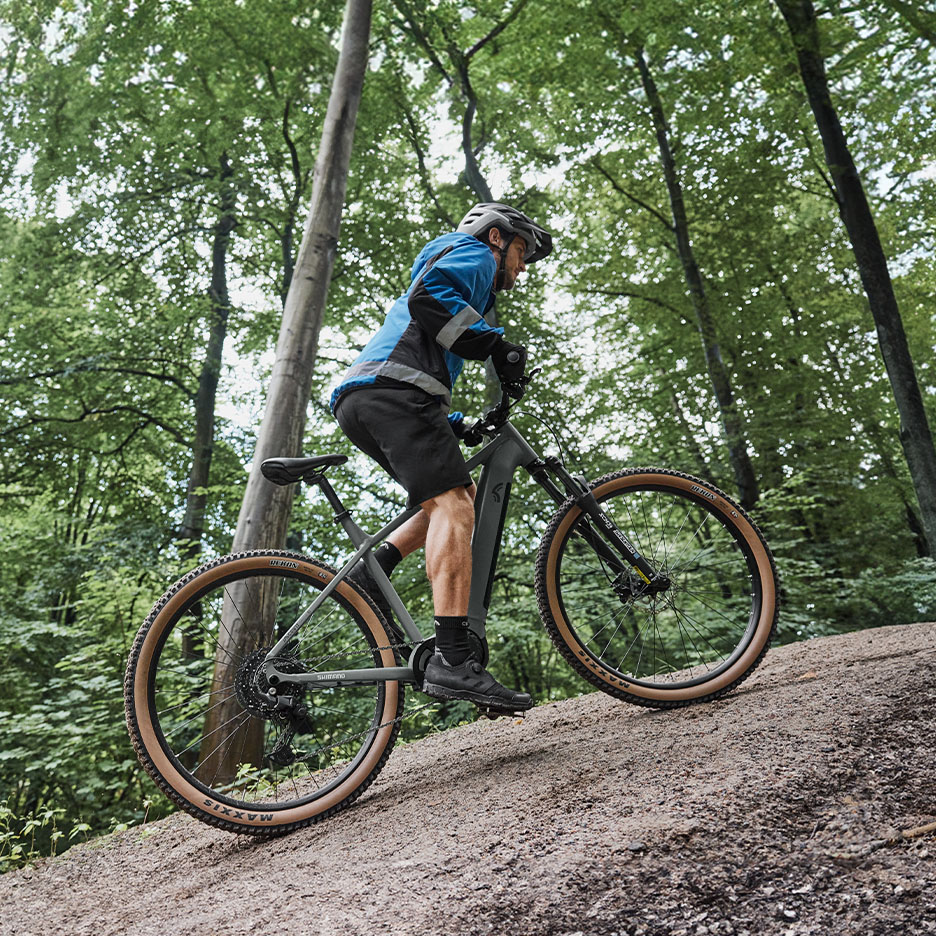 Mann fährt E-Mountainbike bergauf durch einen Wald.