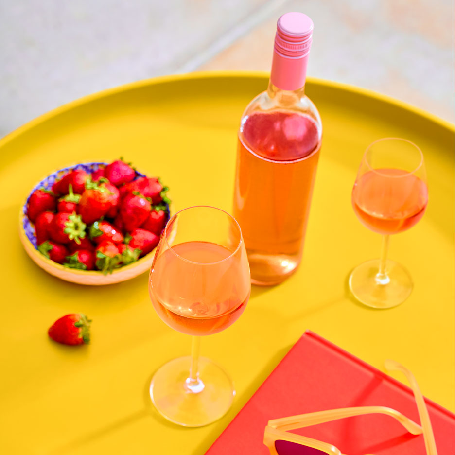 Roséweinflasche und Gläser mit frischen Erdbeeren auf einem gelben Tablett.