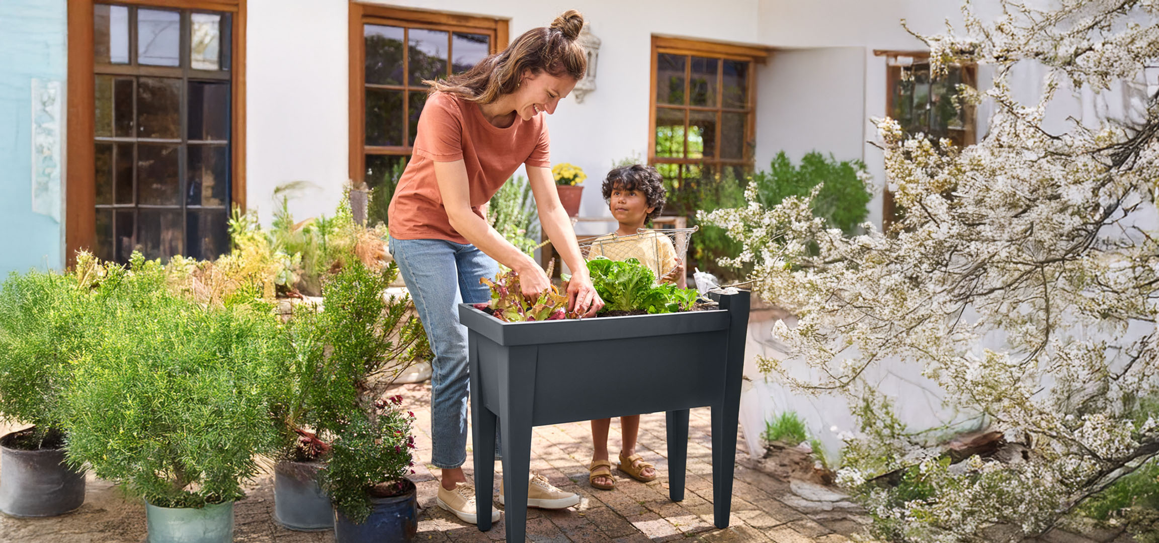 Eine Mutter und ihr Kind pflanzen Gemüse in ein dunkelgraues Hochbeet.