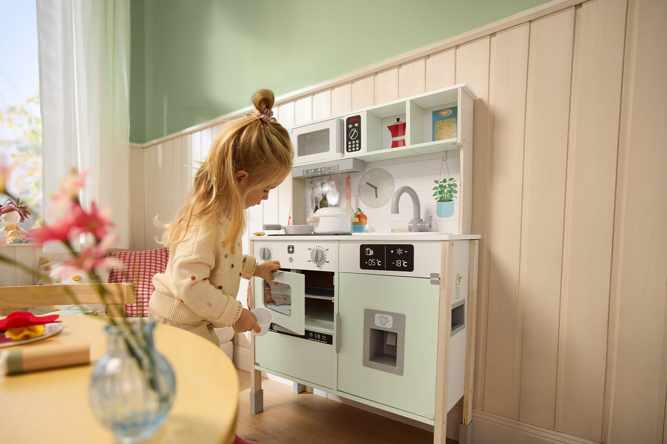 Kleines Mädchen spielt mit einer Holzküche, öffnet die Ofentür.