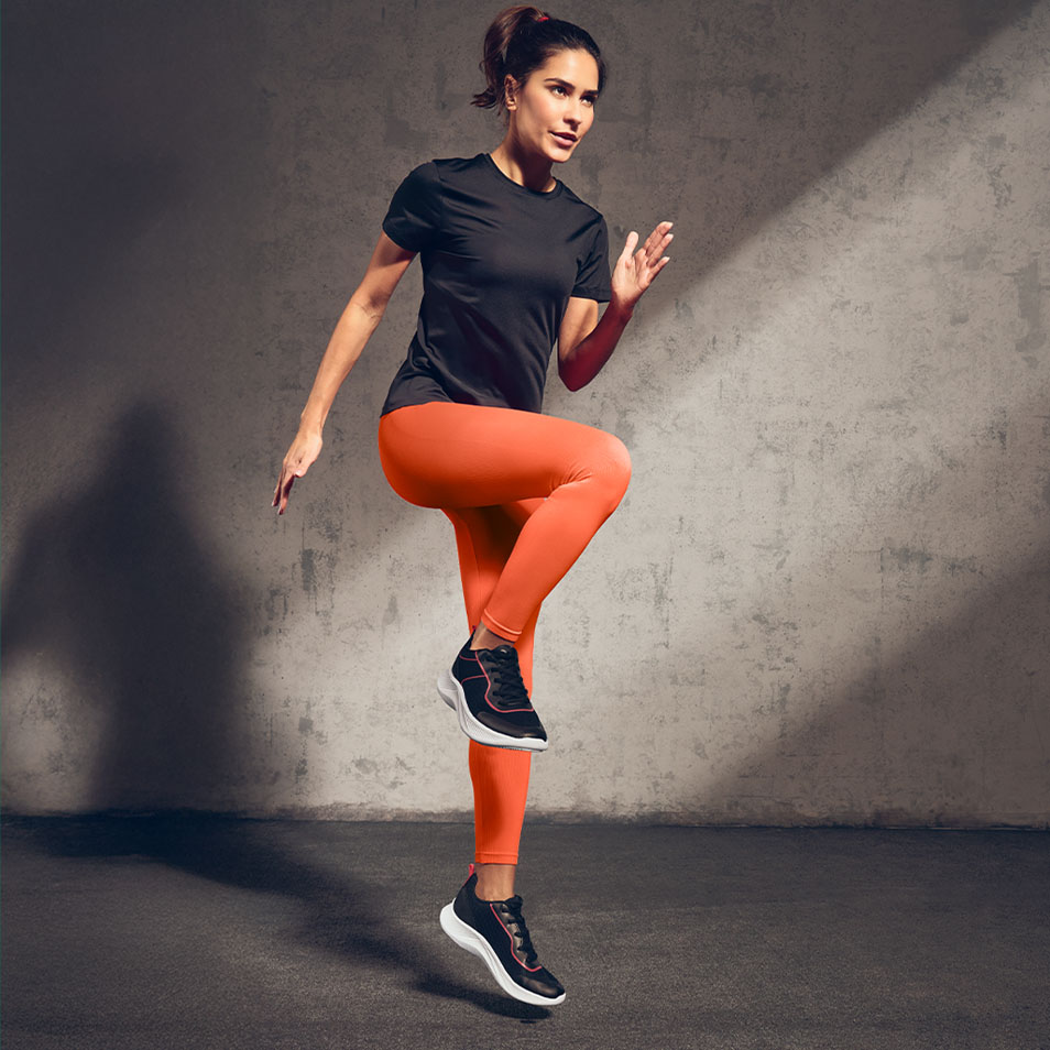 Frau in schwarzem T-Shirt und orangefarbenen Leggings trainiert im Fitnessstudio.