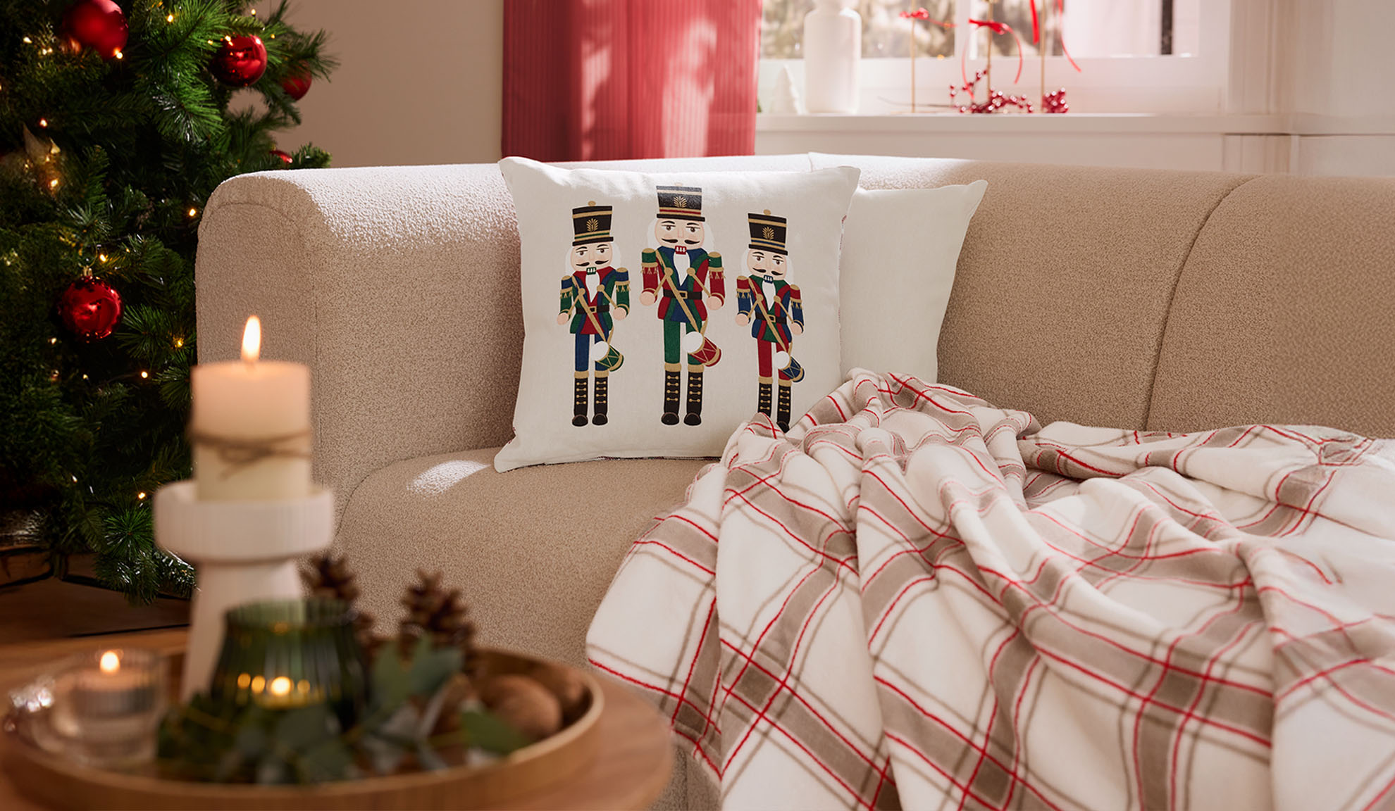 Weihnachtliches Wohnzimmer mit Sofa, Nussknacker-Kissen, karierter Decke und Kerzen.