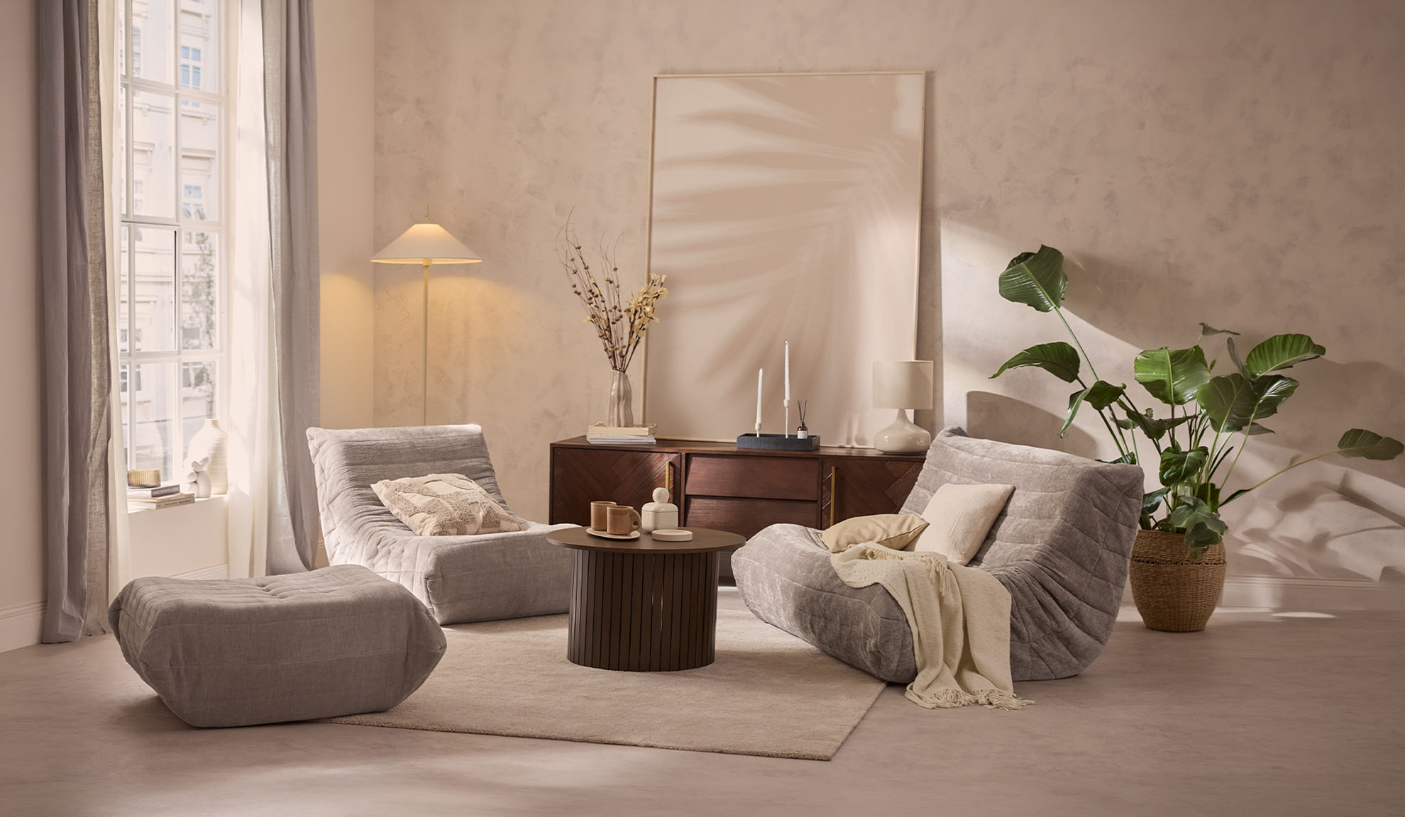 Gemütliches Wohnzimmer mit zwei grauen Loungesesseln, einem Hocker, Couchtisch und Pflanze.